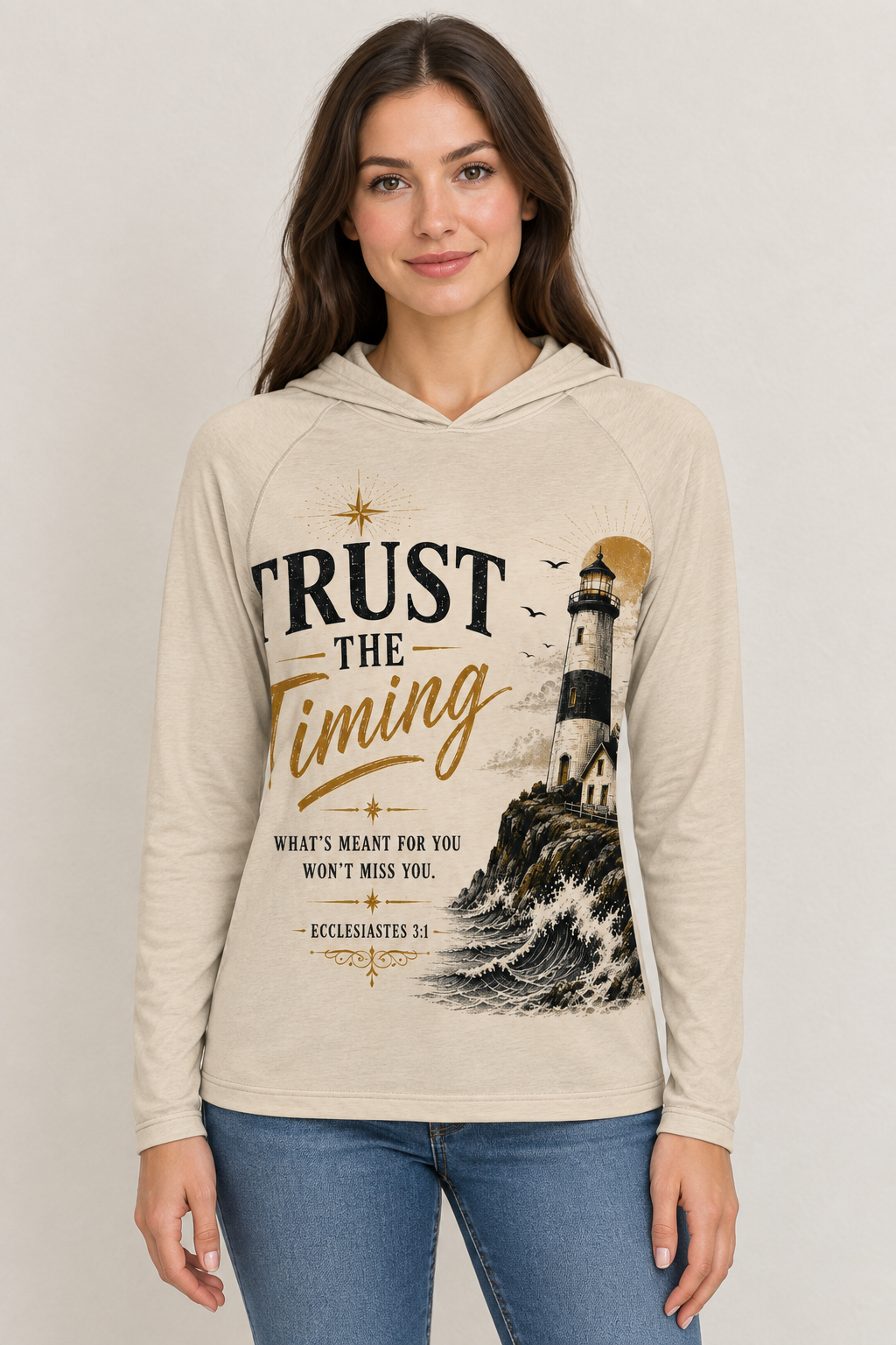 AI-generated mockup of a woman wearing a beige Trust the Timing Christian hooded shirt with lighthouse and wave artwork and blue jeans.
