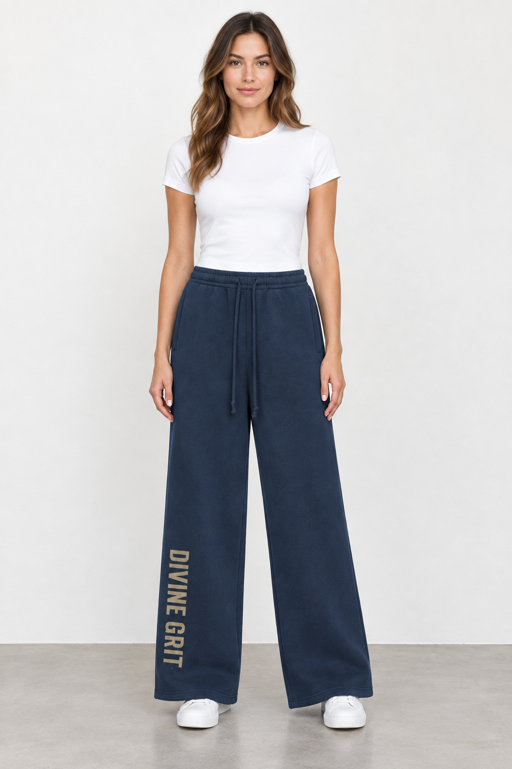 AI-generated mockup of a woman wearing Navy Blue Divine Grit wide-leg fleece sweatpants with vertical gold-toned lettering, a white tee and sneakers.