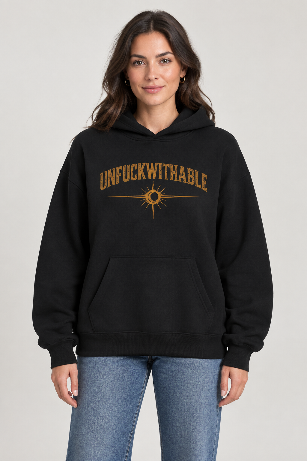 Woman wearing a black oversized hoodie with gold Unfuckwithable lettering and sunburst on the front.