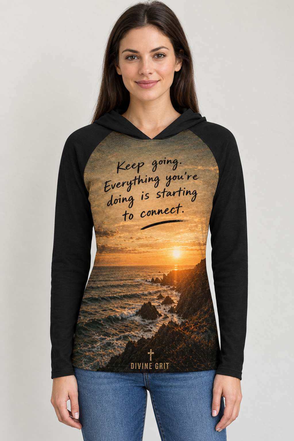 AI-generated mockup of a woman wearing a black hooded shirt with golden coastal sunset artwork and Keep Going Starting to Connect lettering.
