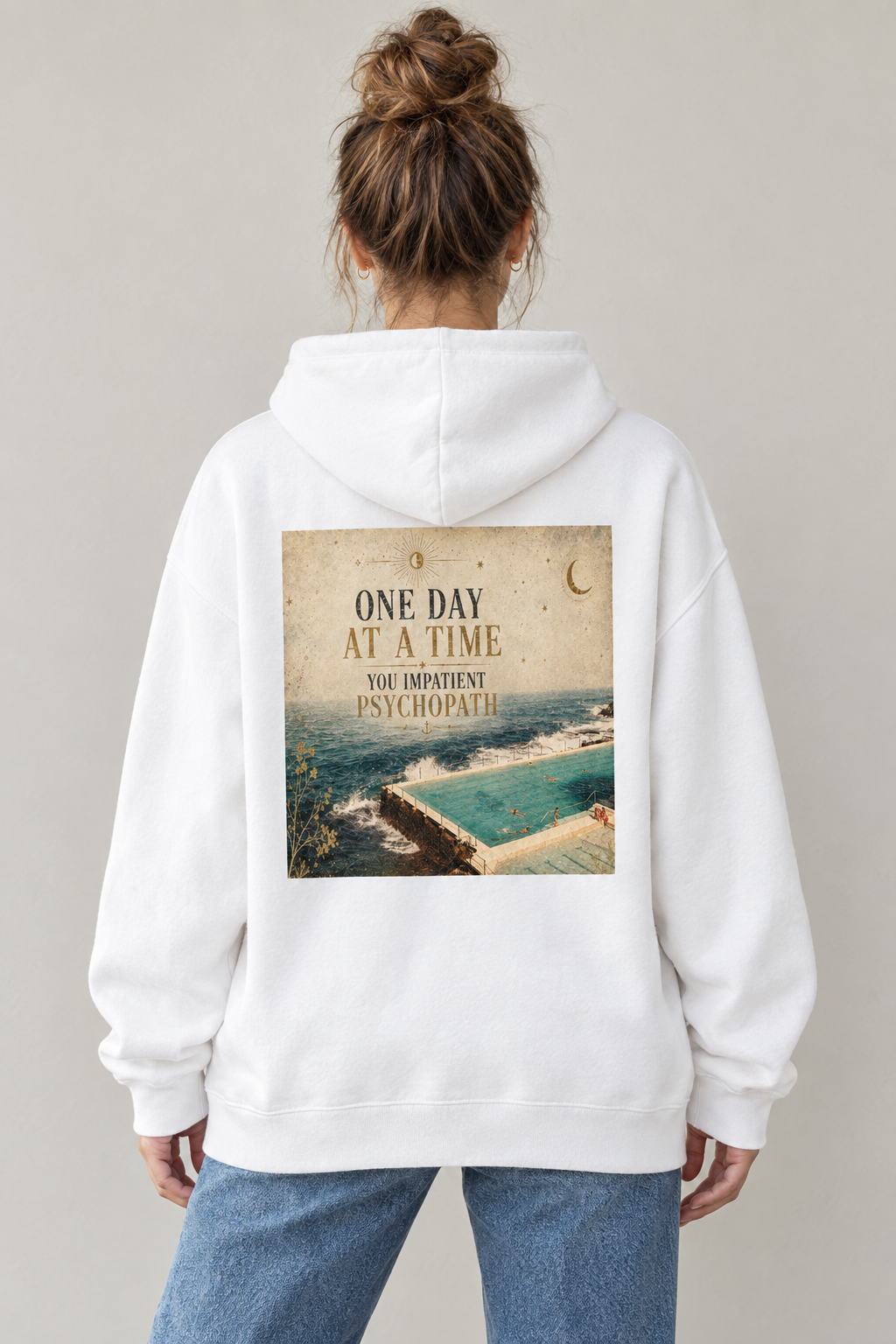 AI-generated back-view mockup of a woman wearing the White One Day at a Time graphic hoodie with coastal pool artwork.