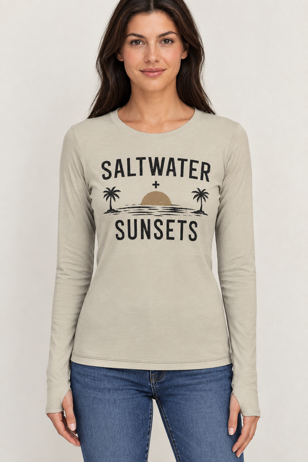 AI-generated mockup of a woman wearing a beige Saltwater and Sunsets long-sleeve shirt with palm-tree sunset artwork, thumbhole cuffs and blue jeans.