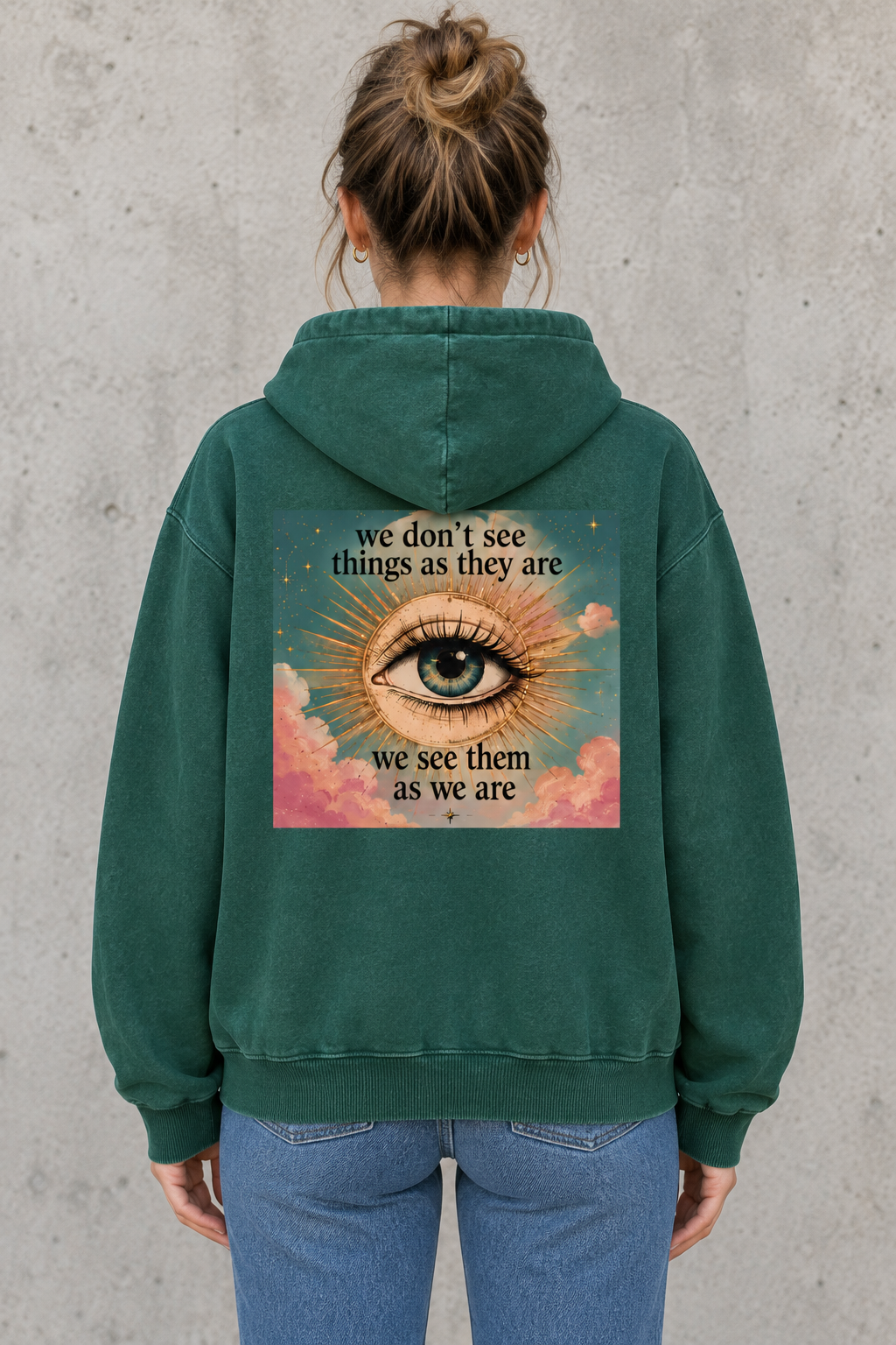 AI-generated mockup of a woman showing the eye, pastel clouds, and perspective quote on the green Eye As We Are hoodie.